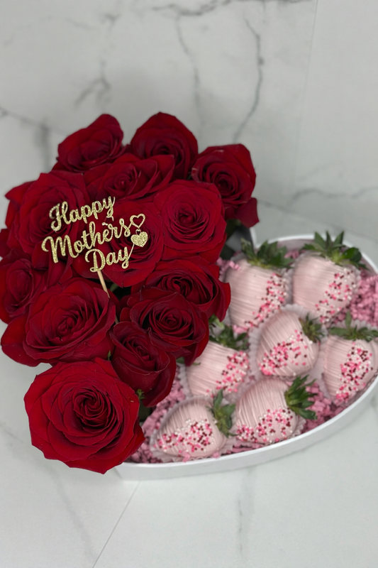 Bouquet of red roses with a 'Happy Mother's Day' card, surrounded by pink strawberries on a marble surface.